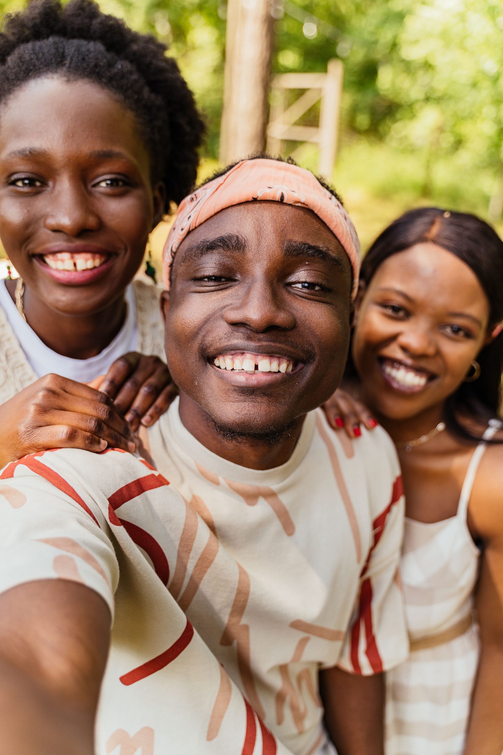 Three friends smiling for a selfie in a green park setting, exuding joy and friendship.
